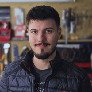 Portret autora poradnika o sprawdzaniu samochodu – ekspert motoryzacyjny w warsztacie, tło z narzędziami